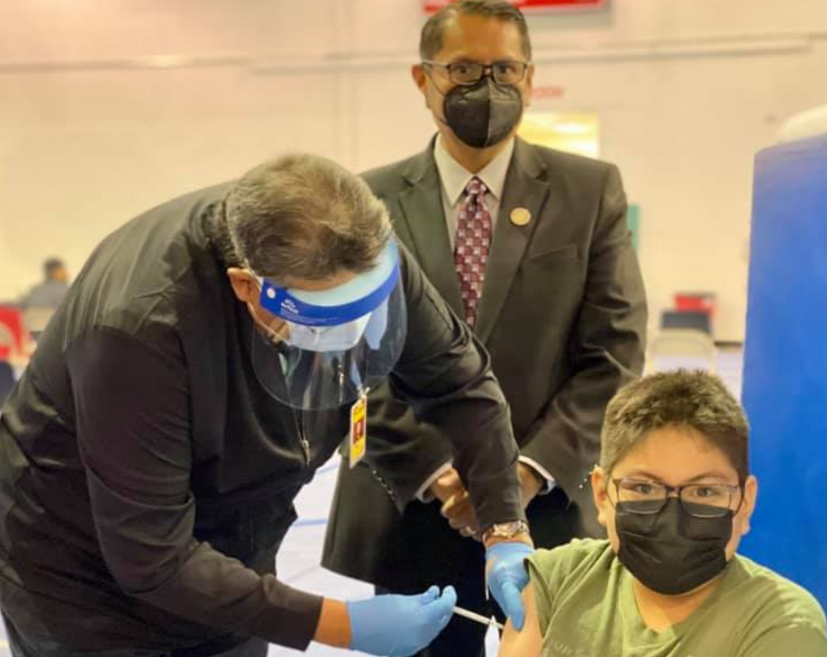 An unidentified Navajo youth gets his Pfizer Covid-19 vaccine shot as Navajo Nation President Jonathan Nez gives him moral support. Courtesy photo from the Navajo Nation