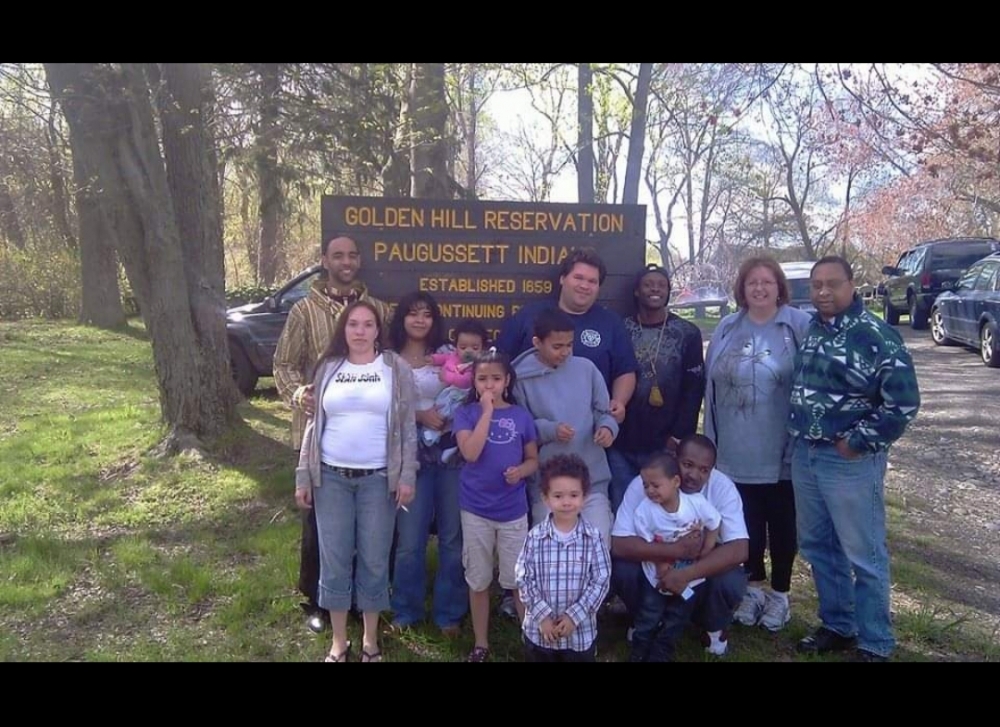 Members of the Golden Hill Paugussett Tribe pose in front of their reservation’s sign in Trumbull, Conn., which spans just a quarter acre. Clan Mother Shoran Waupatukuay Piper stands at front left. (Courtesy Clan Mother Shoran Waupatukuay Piper)